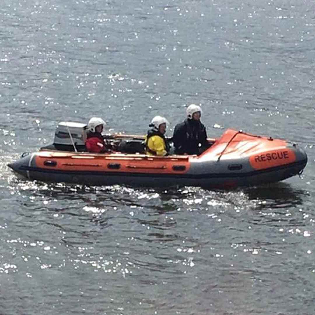 A D class lifeboat with three crew onboard floats on calm seas reflecting sparkles of sunlight