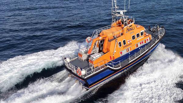 Severn class all-weather lifeboat cruises across calm blue seas in bright sunshine