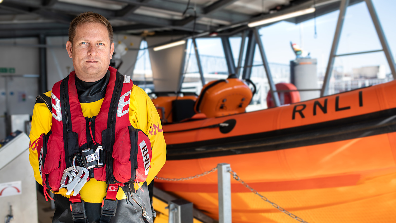Helm Dave Riley is stood next to Poole RNLI's B class lifeboat.