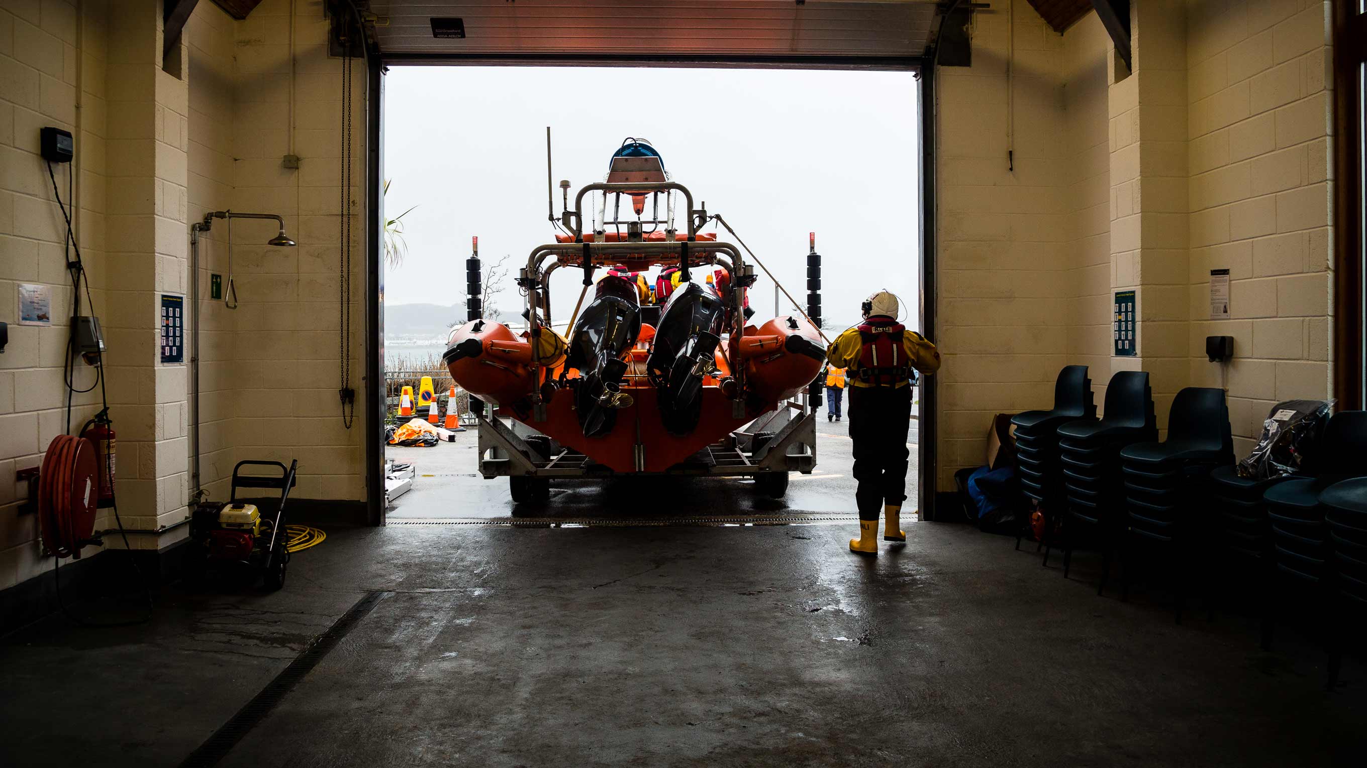 A B class lifeboat on a carriage is towed out of a boathouse with a crew member following close