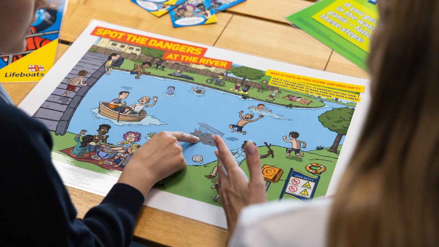 Schoolchildren are looking at a 'spot the dangers at the river' activity, pointing to a hazard in the water. 