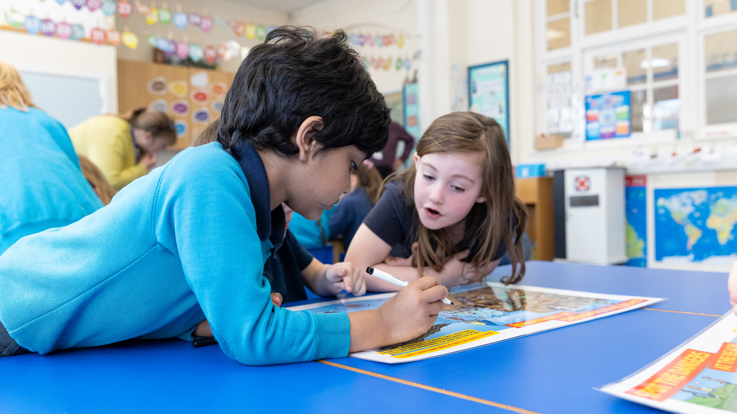 Two young children in a classroom are completing a colourful RNLI worksheet together. 