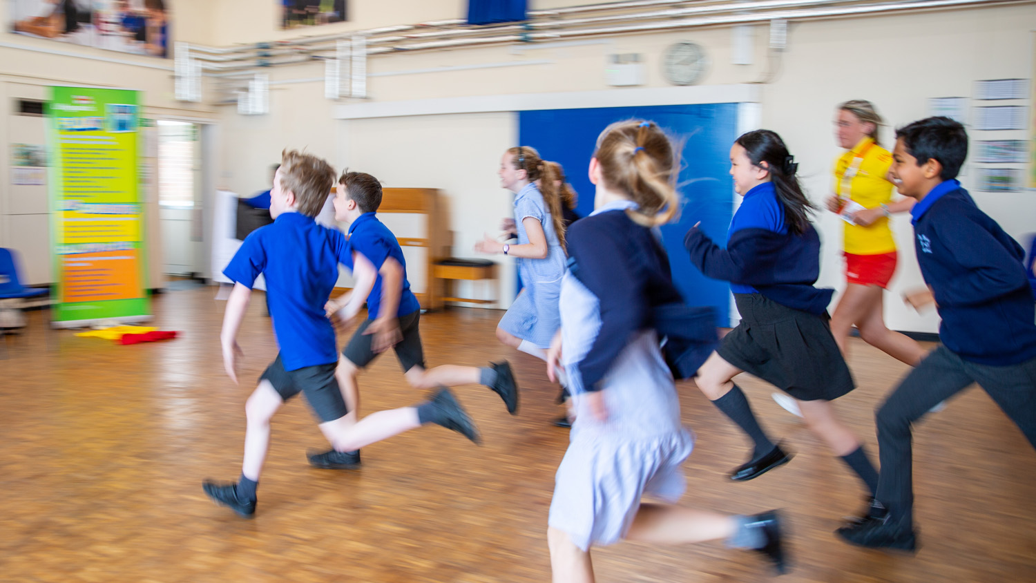 School children running through a school hall with a lifeguard.