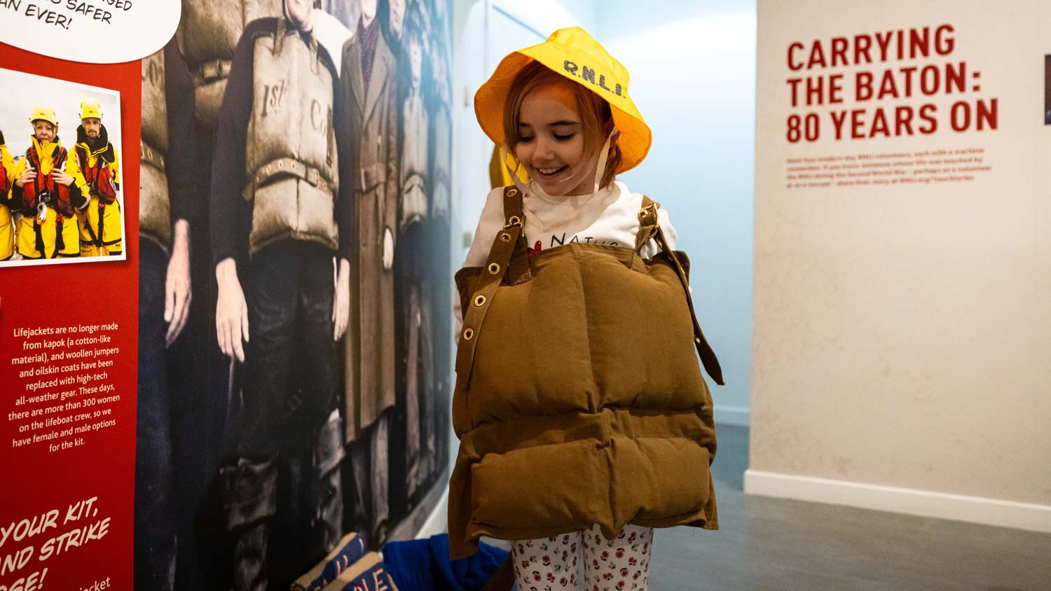 A young girl dresses up in a Second World War era lifejacket and yellow sou'wester hat inside the Stories of Courage exhibition