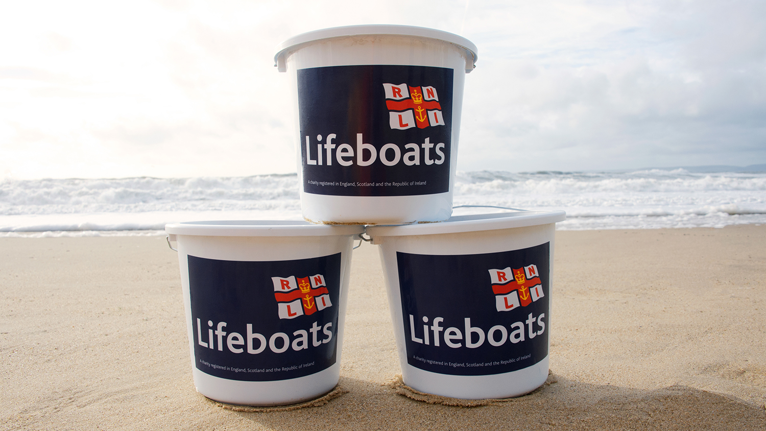 RNLI collecting buckets, piled up on a sandy beach.