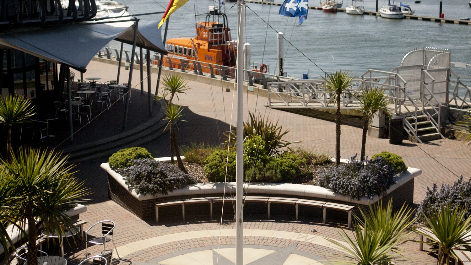 An aerial view of the sea terrace outside the Waterfront Suite at the RNLI College. An all-weather lifeboat can be seen moored on the pontoon. It’s a bright, sunny day.