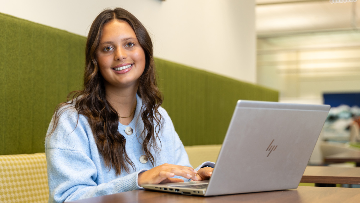 A woman sits at a desk, her laptop is open in front of her